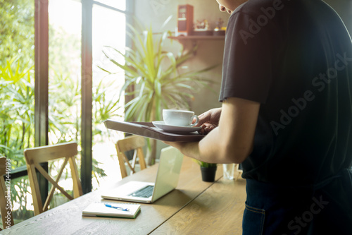 Waiter serving cup of coffee with laptop on the wooden table © bignai