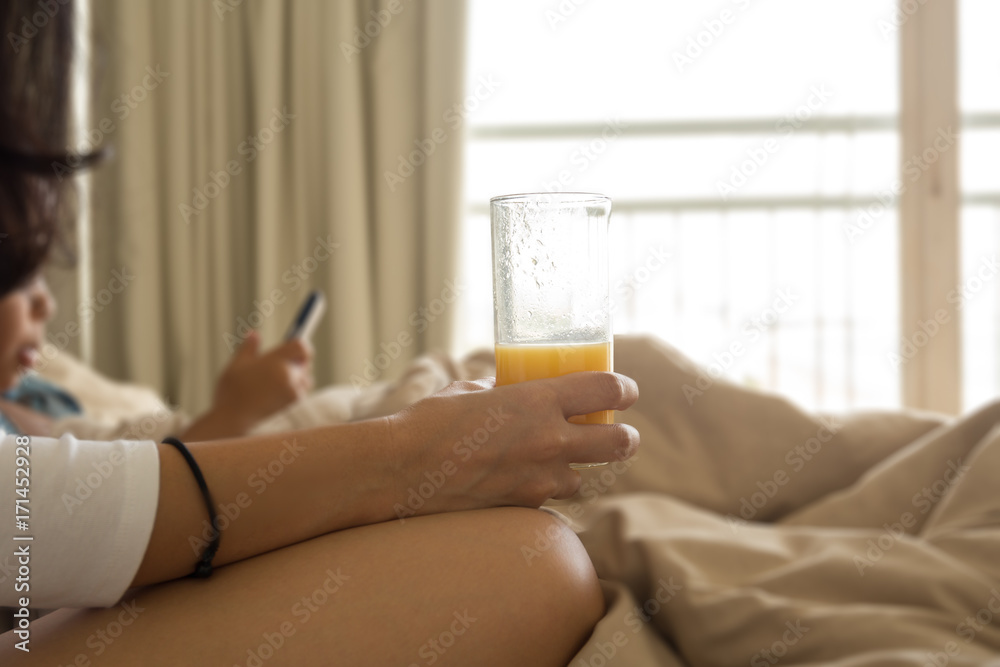 Mother holding glass of orange with son playing cell phone on bed Mother holding glass of orange with son playing cell phone on bed