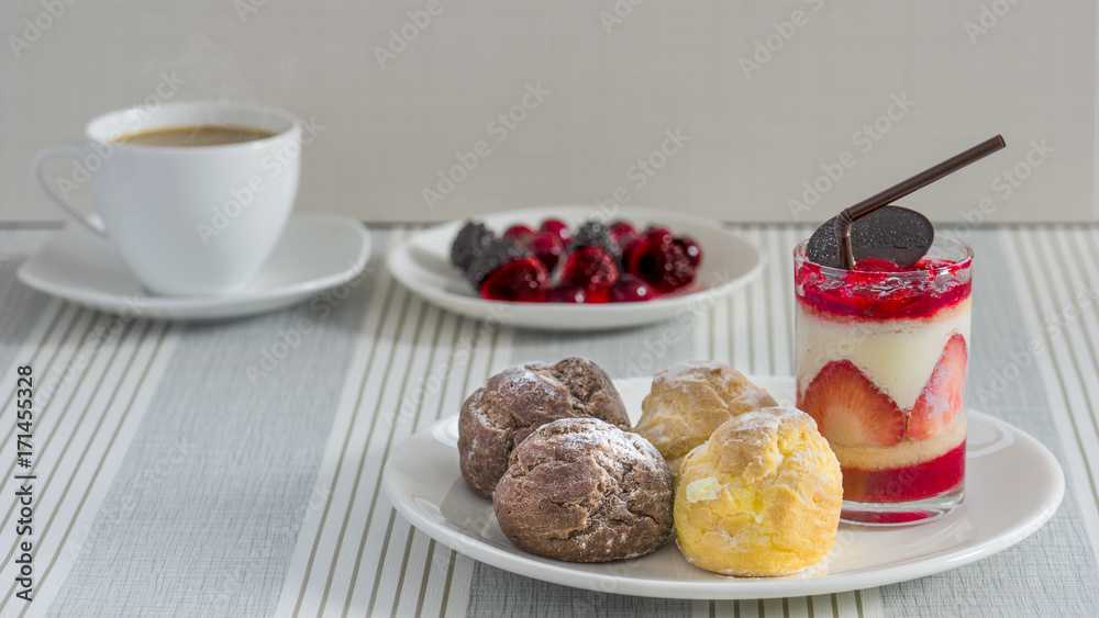 A dish of chou cream and a glass of strawberry chease cake with a cup of tea or coffee and a dish of various berry for an afternoon break. A dish of chou cream and a glass of strawberry chease cake with a cup of tea or coffee and a dish of various berry for an afternoon break.