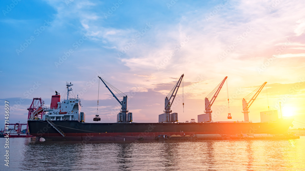 Background for cranes and industrial cargo ships in port at twilight.