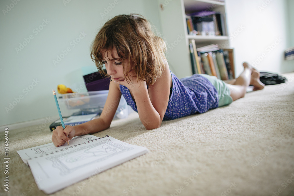 Girl doing homework while lying on floor at home Girl doing homework while lying on floor at home
