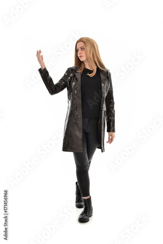 full length portrait of girl wearing black clothes with long leather jacket. standing pose on white background.