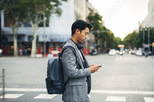 Side view of businessman with backpack using smart phone while standing on street photo