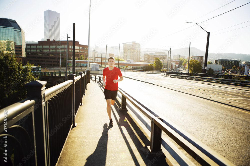 Full length of man jogging on footpath in city during sunny day Full length of man jogging on footpath in city during sunny day