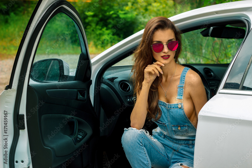 beautiful lady with sexual breasts in a jeans suit poses in the car