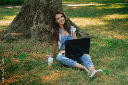 beautiful smiling brunette sits on green grass with laptop