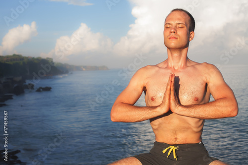 Handsome man doing yoga at cliff with blue sea background