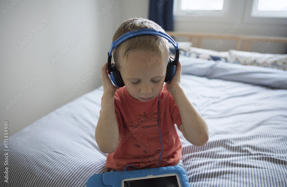 Boy listening music while sitting on bed at home