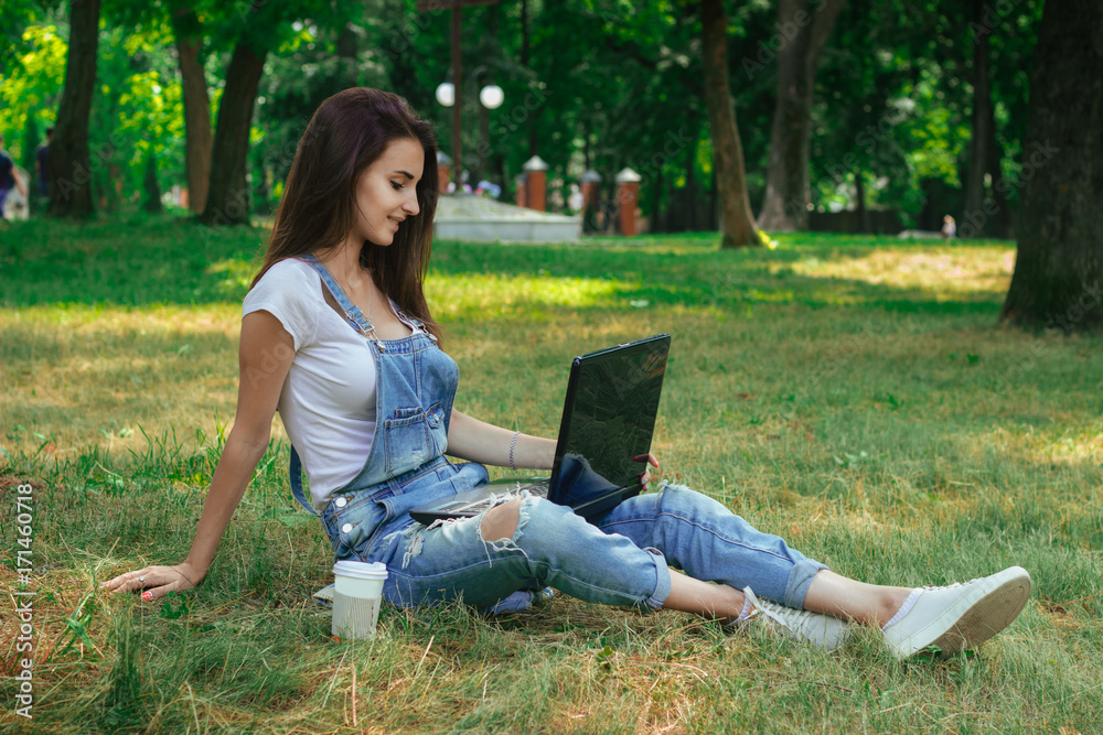 cute women sitting on the grass and looking at laptop