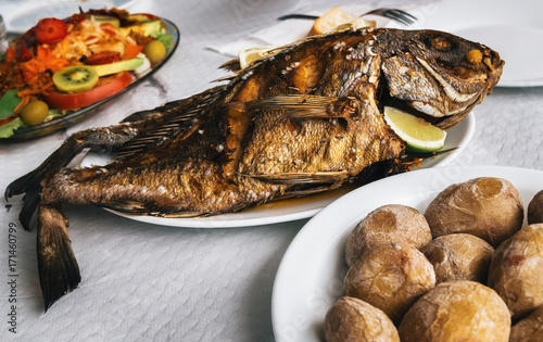 Grilled fish on plate, canarian wrinkly potatoes and salad with vegetables and fruits. Tenerife, Canary islands photo