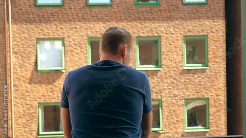 Lonely man standing on his balcony looking at the view on a sunny summer morning.