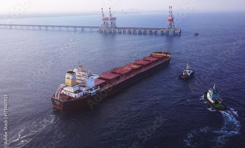 Large bulk carrier ship pulled by tugboats in open water