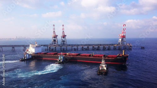 Large bulk carrier ship pulled by tugboats in open water