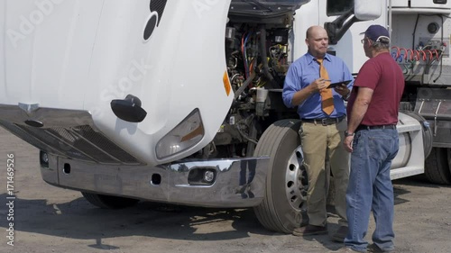 Insurance agent, or other official with electronic notepad, talks to truck driver during an inspection of truck engine. Full length view from front angle. Hand-held 4K