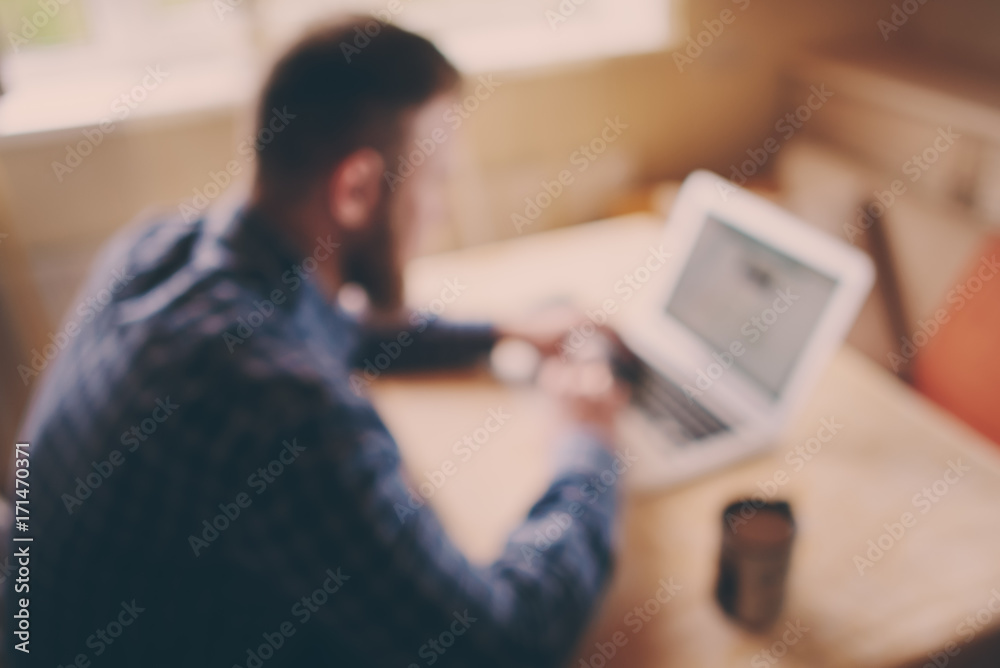 blurred background, businessman using laptop at workplace - rear view