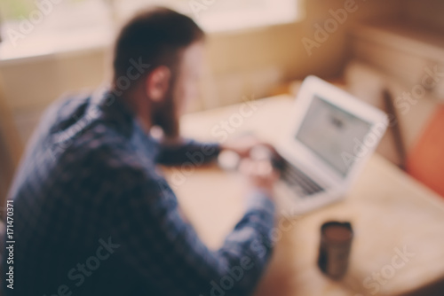 blurred background, businessman using laptop at workplace - rear view