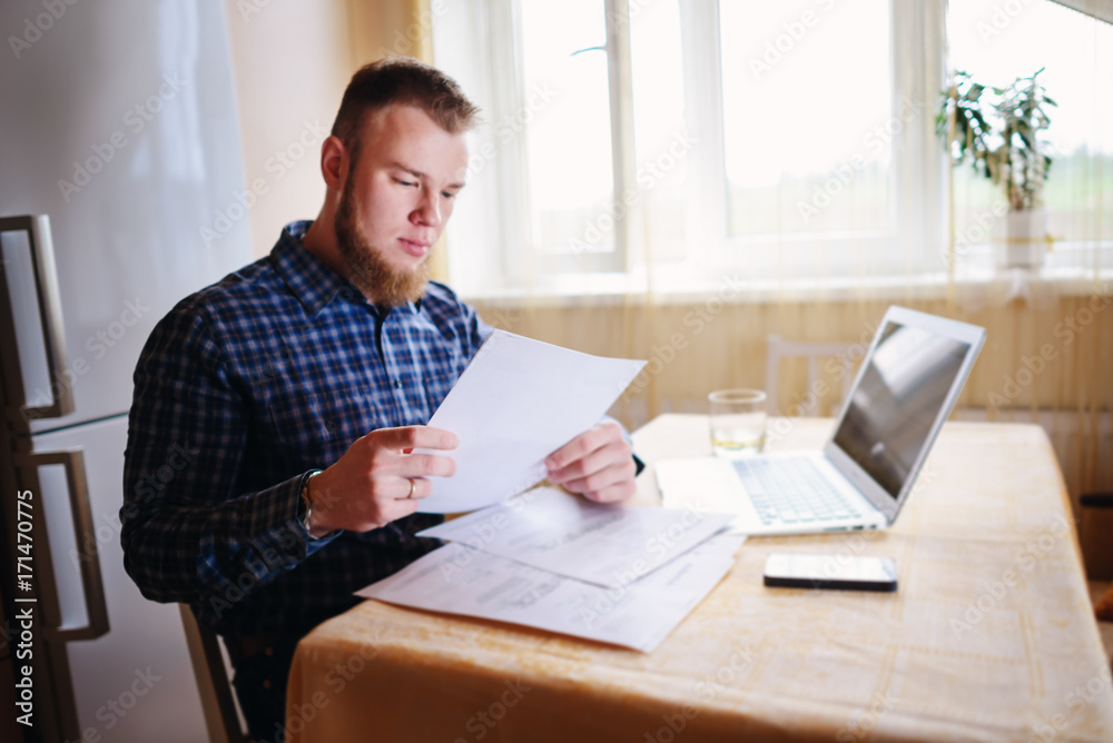 Businessman at home, he is working with a laptop, checking paperwork and bills Businessman at home, he is working with a laptop, checking paperwork and bills