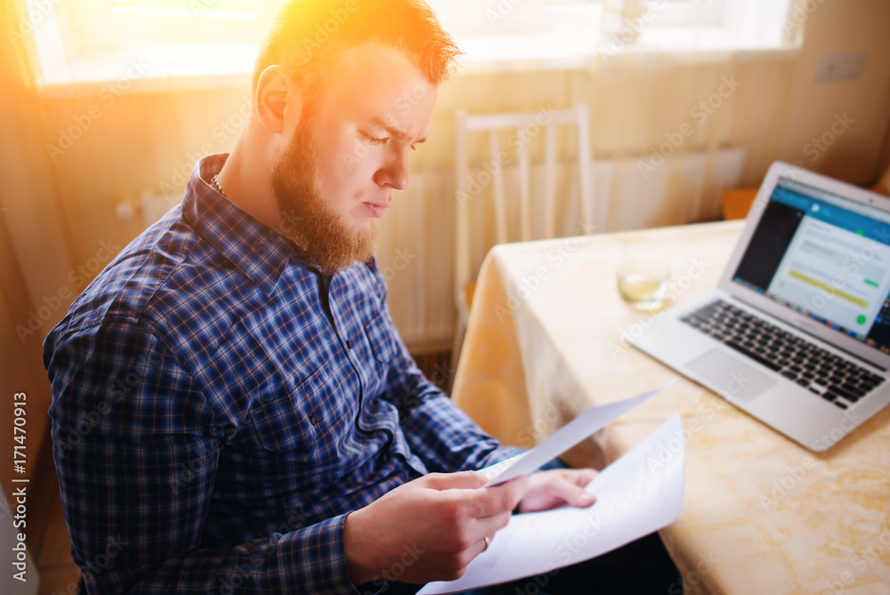 Businessman at home, he is working with a laptop, checking paperwork and bills