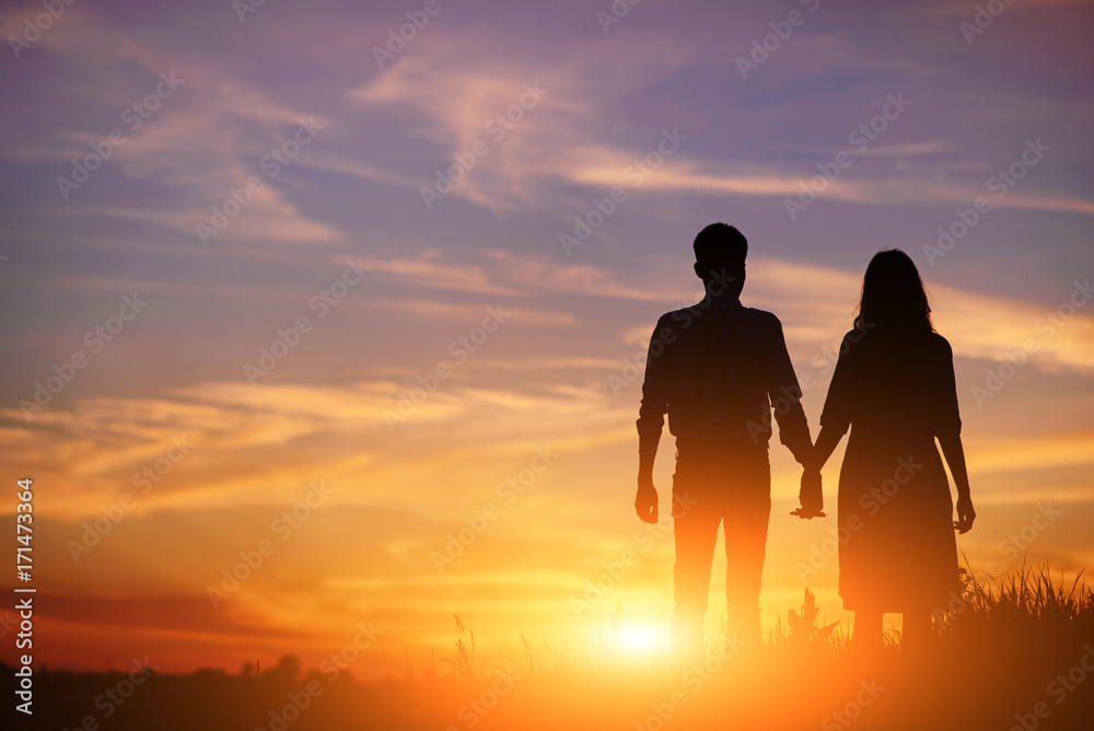 young couple is holding hands on a background sunset silhouette