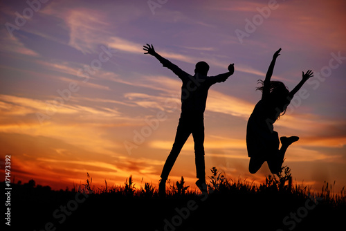 A young man with his girlfriend jump on background sunset silhouette
