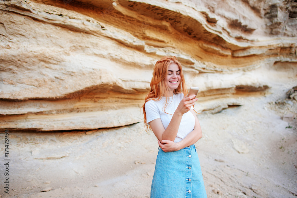 Beautiful woman smiling and looking at the screen of a smartphone on the background of a sand quarry Beautiful woman smiling and looking at the screen of a smartphone on the background of a sand quarry