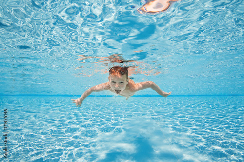 Happy young boy swim and dive underwater, kid breast stroke with fun in pool. Active healthy lifestyle, water sport activity and lessons with parents on summer family vacation with child