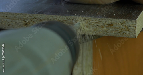 Man holds a drill in his hands and makes a hole in a wooden board. Wood shavings flying around. Close up photo