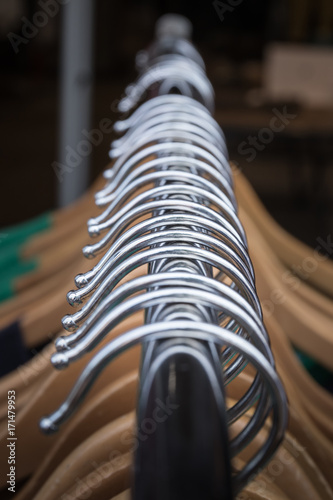 Closeup of clothes on hangers on a rack for a store, emphasizing the metal parts of the hangers that pass through the picture in a symmetrical line giving an abstract feeling to the whole.