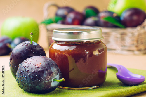 Jar with baby food plum puree with spoon near fresh plums