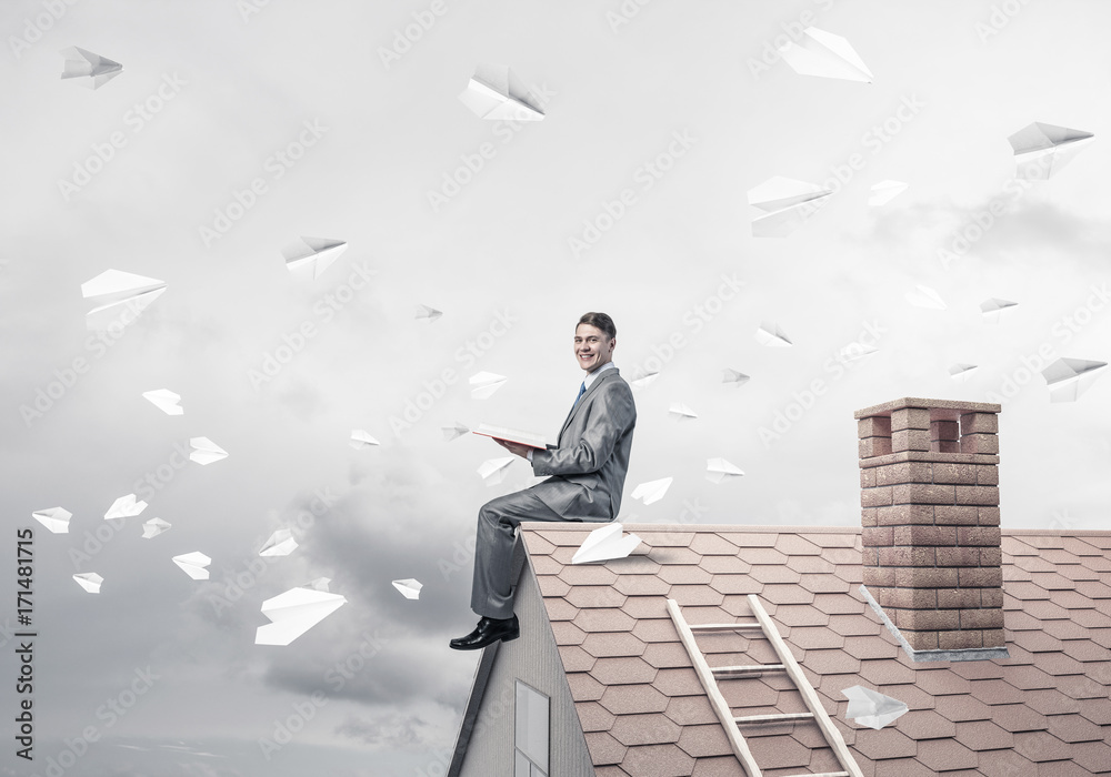 Man on brick roof reading book and paper planes flying in air Man on brick roof reading book and paper planes flying in air