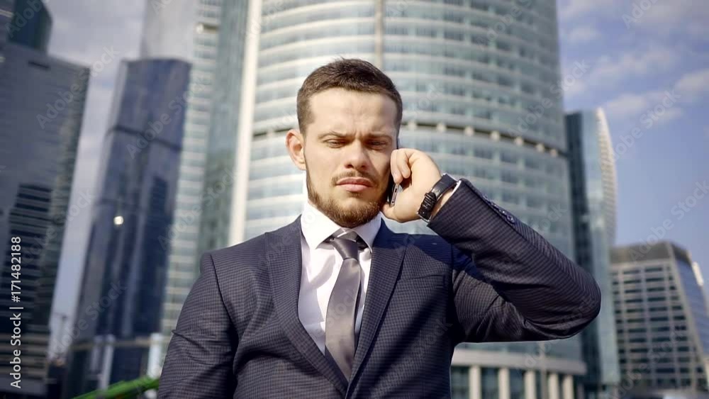 Serious young handsome businessman is talking on a phone with a office and making deals. Serious young handsome businessman is talking on a phone with a office and making deals.