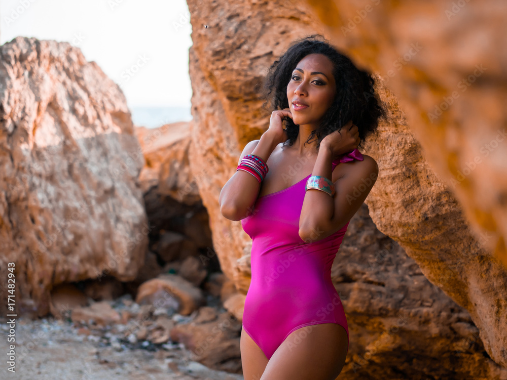 Portrait of cheerful black people, pretty happy young african american woman smiling. Rocks beach. Sexy girl in pink swimsuit and jewelry enjoying nature. Travel, holiday concept. Portrait of cheerful black people, pretty happy young african american woman smiling. Rocks beach. Sexy girl in pink swimsuit and jewelry enjoying nature. Travel, holiday concept.
