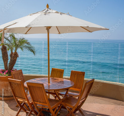 Oceanfront Patio   Wood table  chairs and umbrella on a large patio overlooking the blue ocean waters.