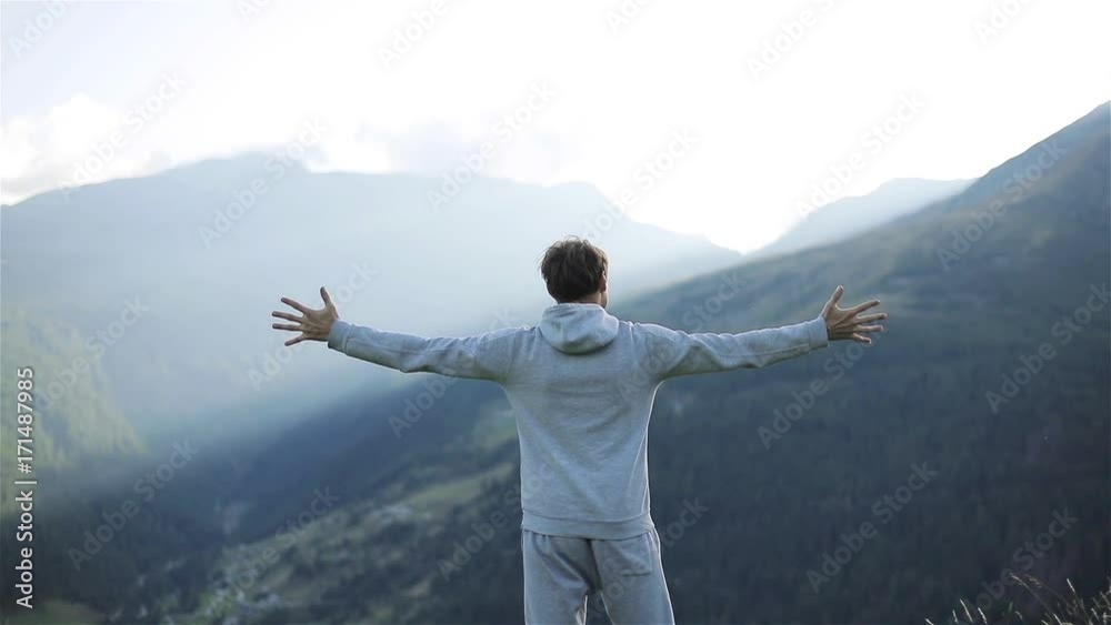 Man raises hands up standing back on mountain top morning sun shine slow motion. No face male silhouette figure in sportswear enjoying life above world. Achievement success motivation winner concept
