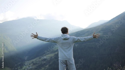 Man raises hands up standing back on mountain top morning sun shine slow motion. No face male silhouette figure in sportswear enjoying life above world. Achievement success motivation winner concept photo