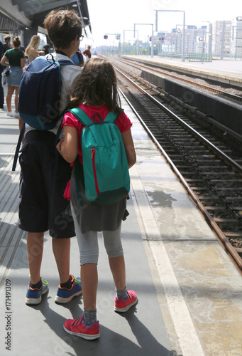 brother and sister with backpacks waiting ata station photo