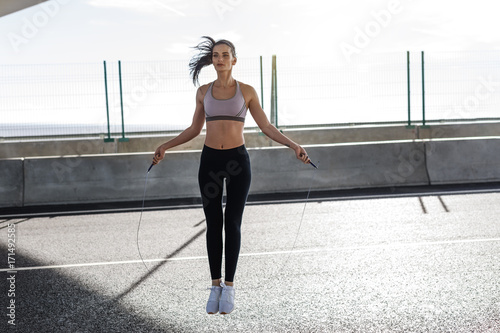 Young fit woman skipping with a jump rope in the city, full length  photo