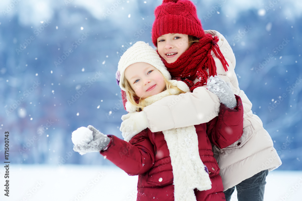 Two adorable little girls having fun together in beautiful winter park. Beautiful sisters playing in a snow. Two adorable little girls having fun together in beautiful winter park. Beautiful sisters playing in a snow.