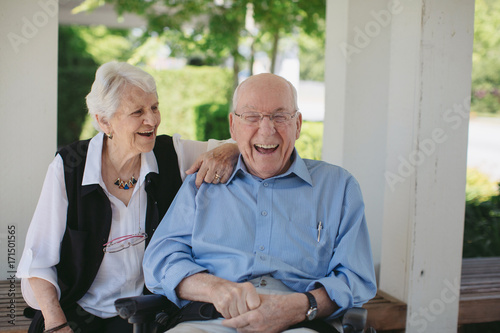 Happy, fun loving elderly couple outside in garden using wheelchair