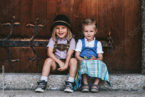 cute smiling children couple in dirndl dress and lederhosen  in front of wooden door photo