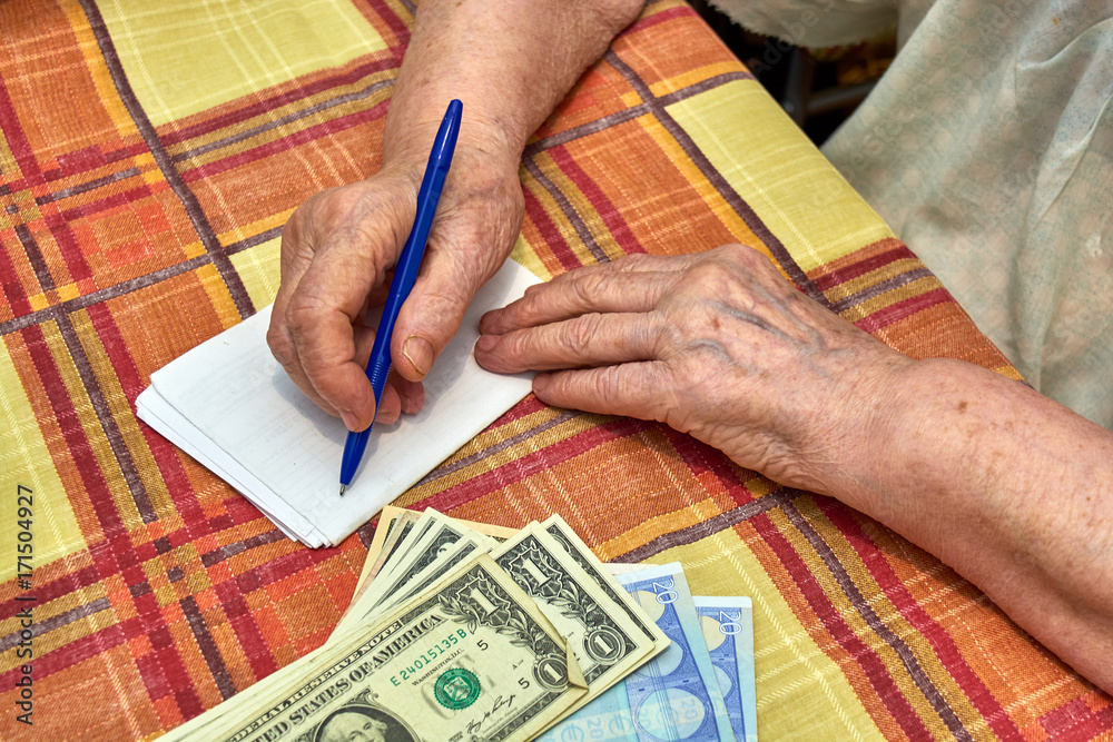 An elderly woman writes down expenses in notepad