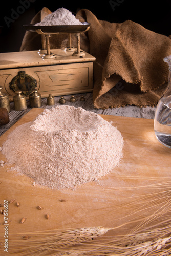 Fontana di farina bianca sulla spianatoia di legno e sul piatto d’ottone di una antica bilancia con i pesi  photo