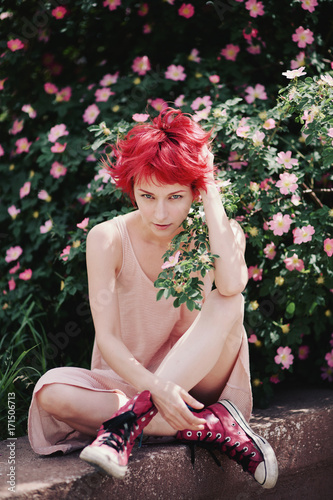 Caucasian female with bright red hair sitting near a flowering briar bush photo