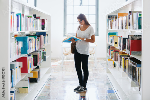 Young university woman reading a book in a library.