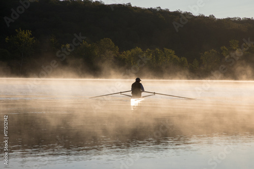 Silhouetted Man Sculling at Sunrise on Water with Fog