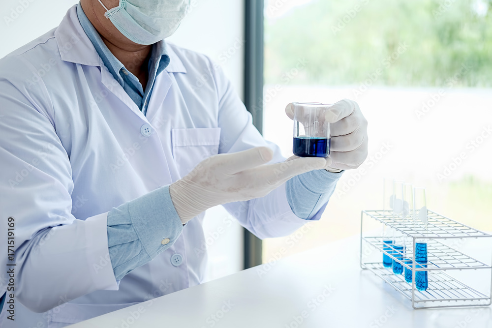 Medical or scientific researcher or man doctor looking at a test tube of clear solution in a laboratory Medical or scientific researcher or man doctor looking at a test tube of clear solution in a laboratory
