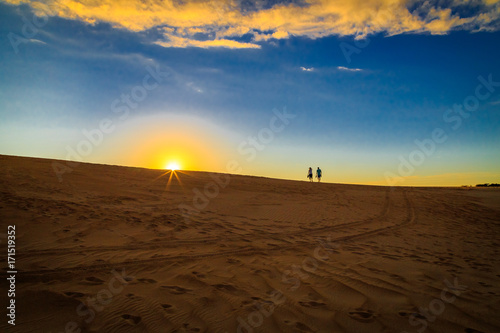 Sunset above sand dunes with couple silhouette
