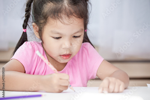 Cute asian child girl having fun to draw and paint with crayon in the room