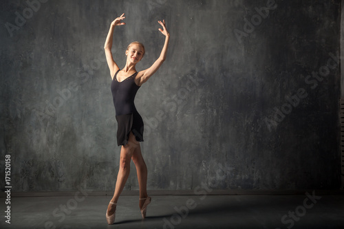 Young beautiful woman prima theater in a black pack, white pantyhose, white pointe shoes beautifully dances Russian ballet in a black dance studio