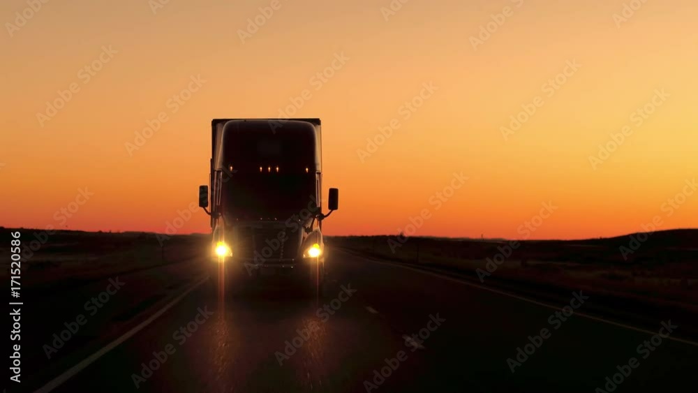 CLOSE UP: Freight container trailer truck transporting goods driving along the multiple lane country highway in Great Plains at sunset. Lorry traveling across the USA at dramatic golden light dusk